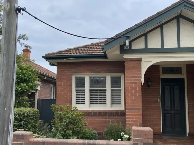 Overhead service cable and point-of-attachment bracket on a brick house with tiled roof in Chatswood
