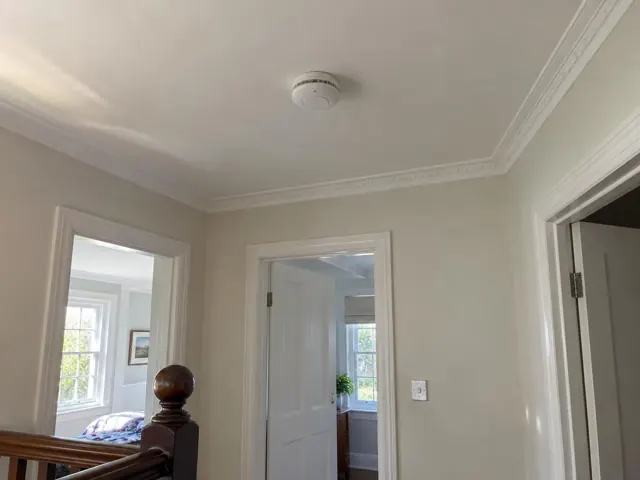 Ceiling smoke alarm in a painted hallway with white trim and doorways in Lane Cove